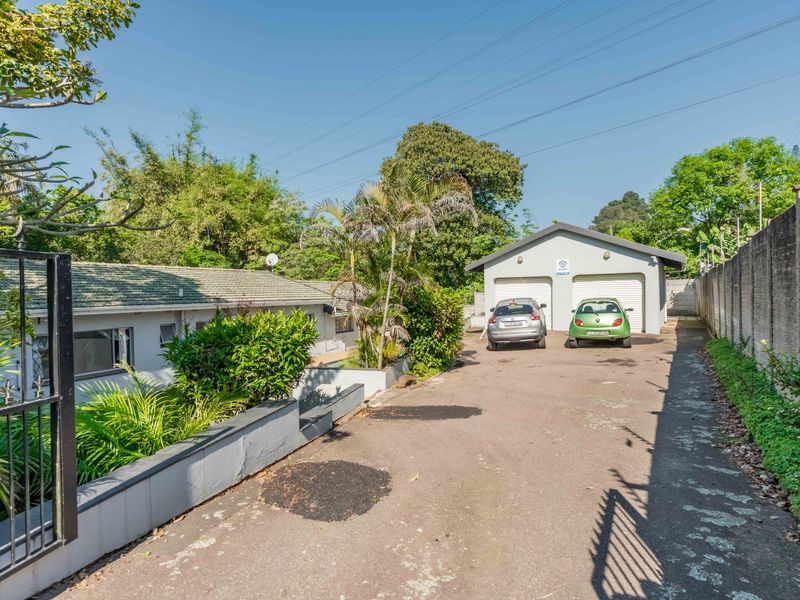 Front view of the property featuring a double garage, paved driveway, and secure perimeter wall with electric fencing.