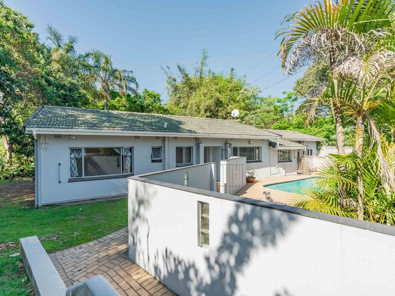 Rear view of the property featuring a swimming pool, paved patio area, and established garden surroundings.