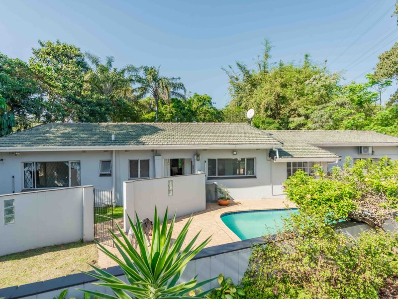 Rear view of the property featuring a swimming pool, paved patio area, and established garden surroundings.