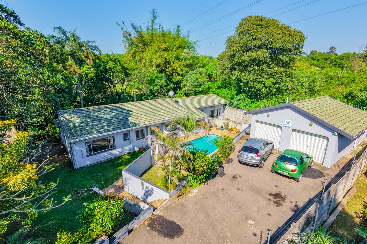 Aerial view of a residential property featuring a main house, swimming pool, and a detached double garage with a paved driveway.