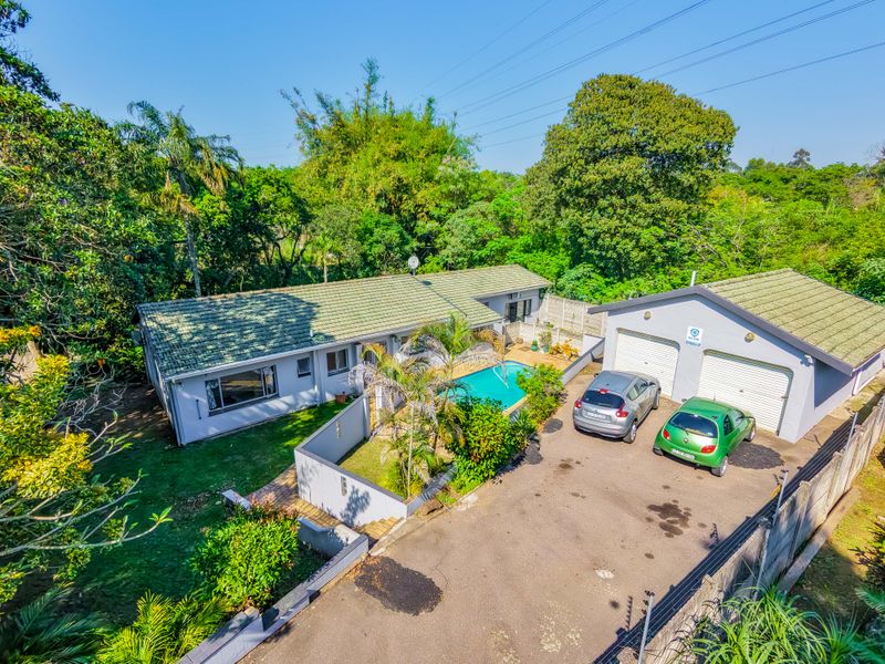 Aerial view of a residential property featuring a main house, swimming pool, and a detached double garage with a paved driveway.