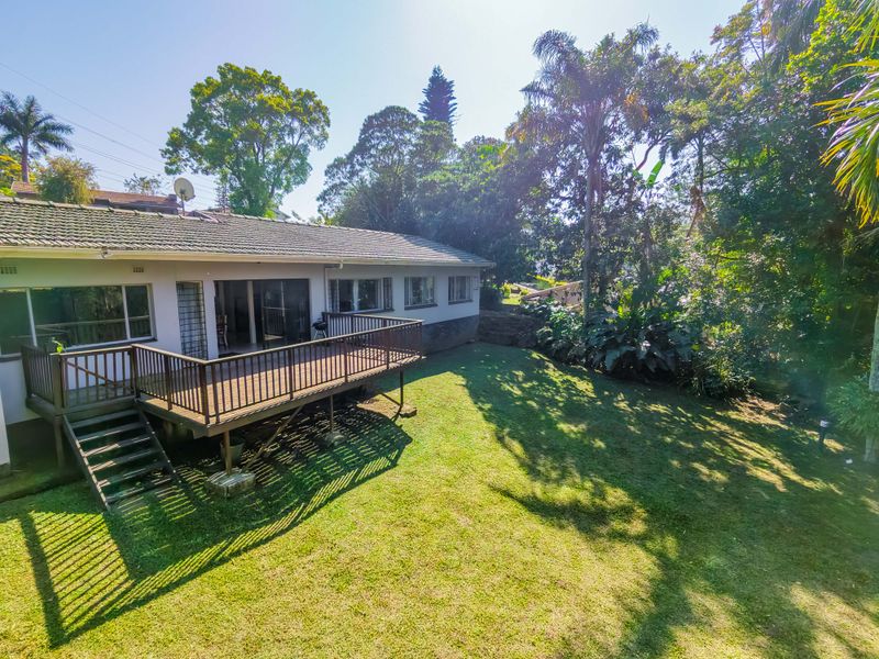 Rear view of the property featuring a raised timber deck, sliding glass doors, and a spacious, well-maintained garden area.