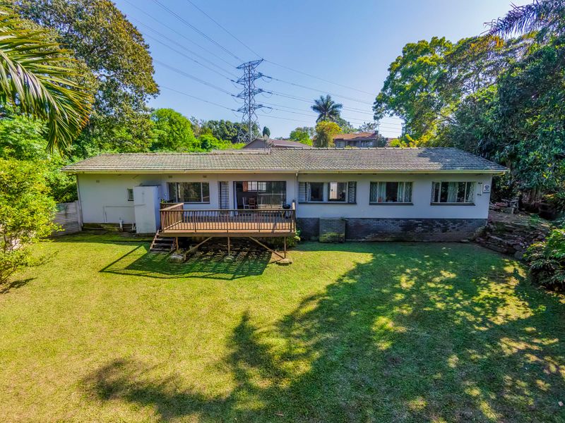 Rear view of the house featuring a timber deck, tiled roof, and a spacious garden area.