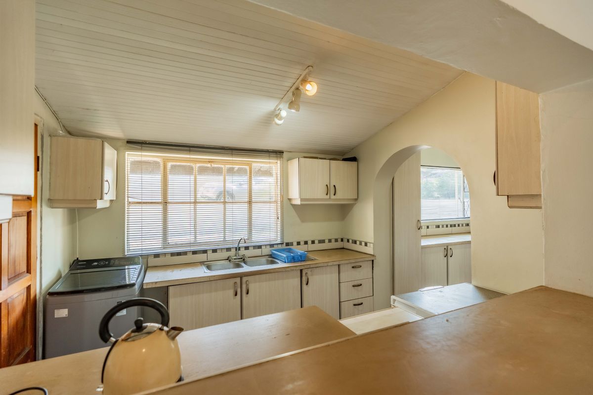 A functional kitchen featuring built-in cabinetry, double basin sink, tiled backsplash, and a distinctive timber ceiling with an arched transition to an adjacent space.