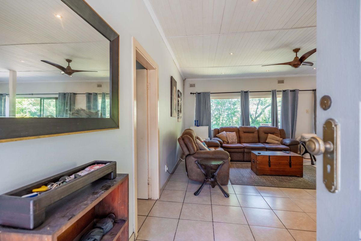 A bright living room featuring tiled flooring, a white tongue and groove ceiling with recessed lighting, and large windows overlooking the garden.