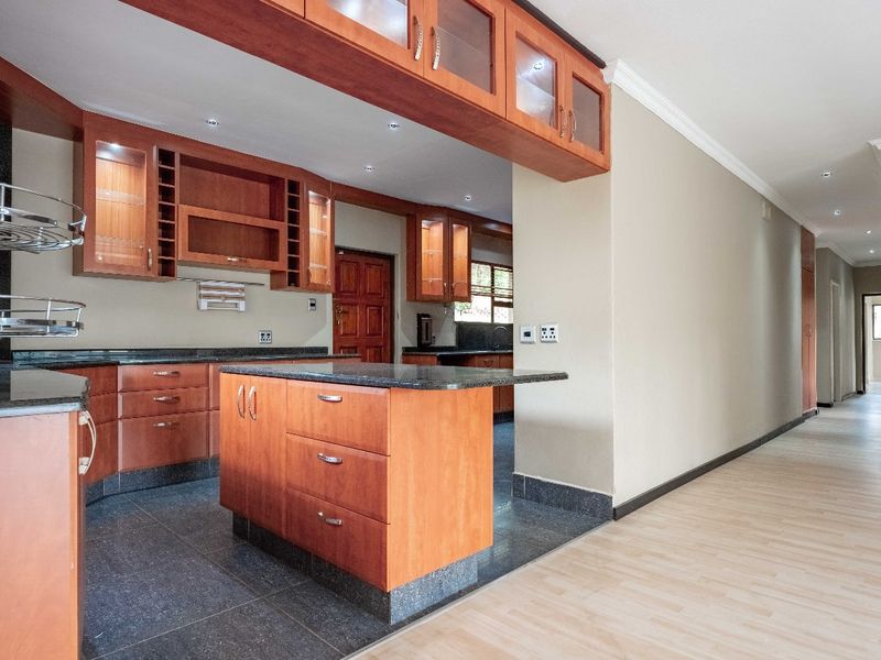 Spacious kitchen featuring wooden cabinetry, granite countertops, and a central island, seamlessly flowing into an adjacent hallway area.