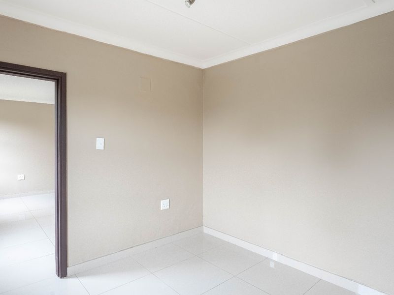 A clean, empty bedroom featuring neutral wall paint, white tiled flooring, and modern finishes, providing a versatile space ready for personalization.