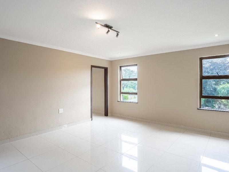 A bright and spacious living area featuring neutral wall tones, polished white floor tiles, and modern aluminium-framed windows.