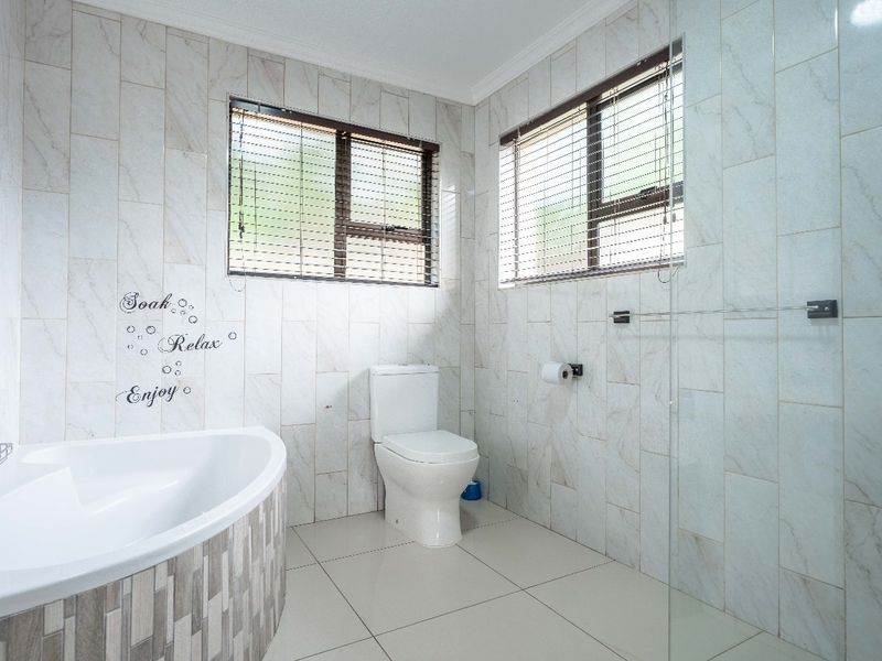 A modern, well-maintained bathroom featuring a corner bathtub, glass shower screen, and neutral floor-to-ceiling wall tiles.