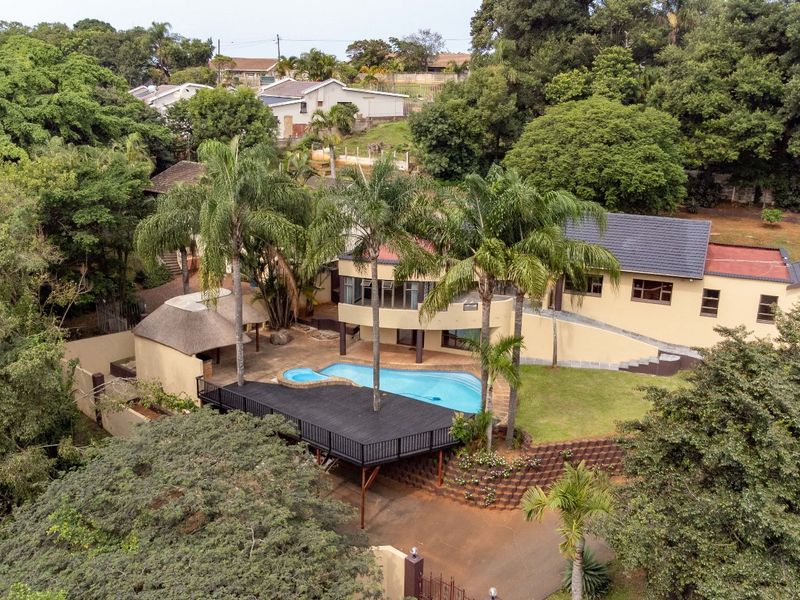 Aerial view of a residential property featuring a swimming pool, raised timber deck, thatched lapa, and landscaped garden area.