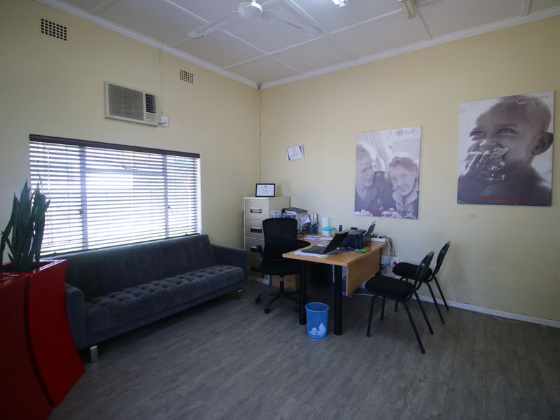 A functional office space featuring laminate flooring, a wall-mounted air conditioning unit, and ceiling fan, suitable for a professional workspace or study.