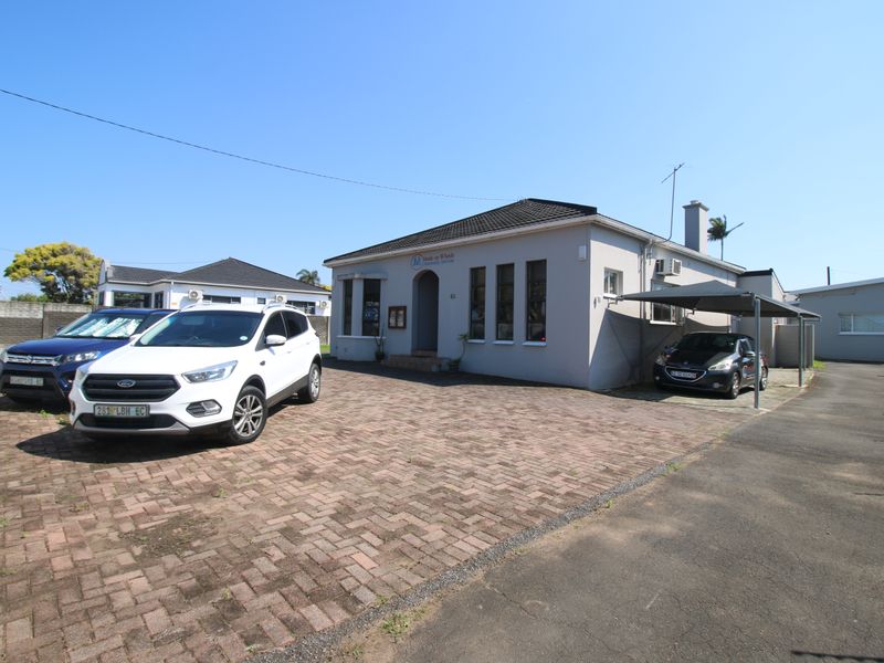 Front exterior view of a single-story house featuring a paved driveway, carport, and perimeter boundary wall.