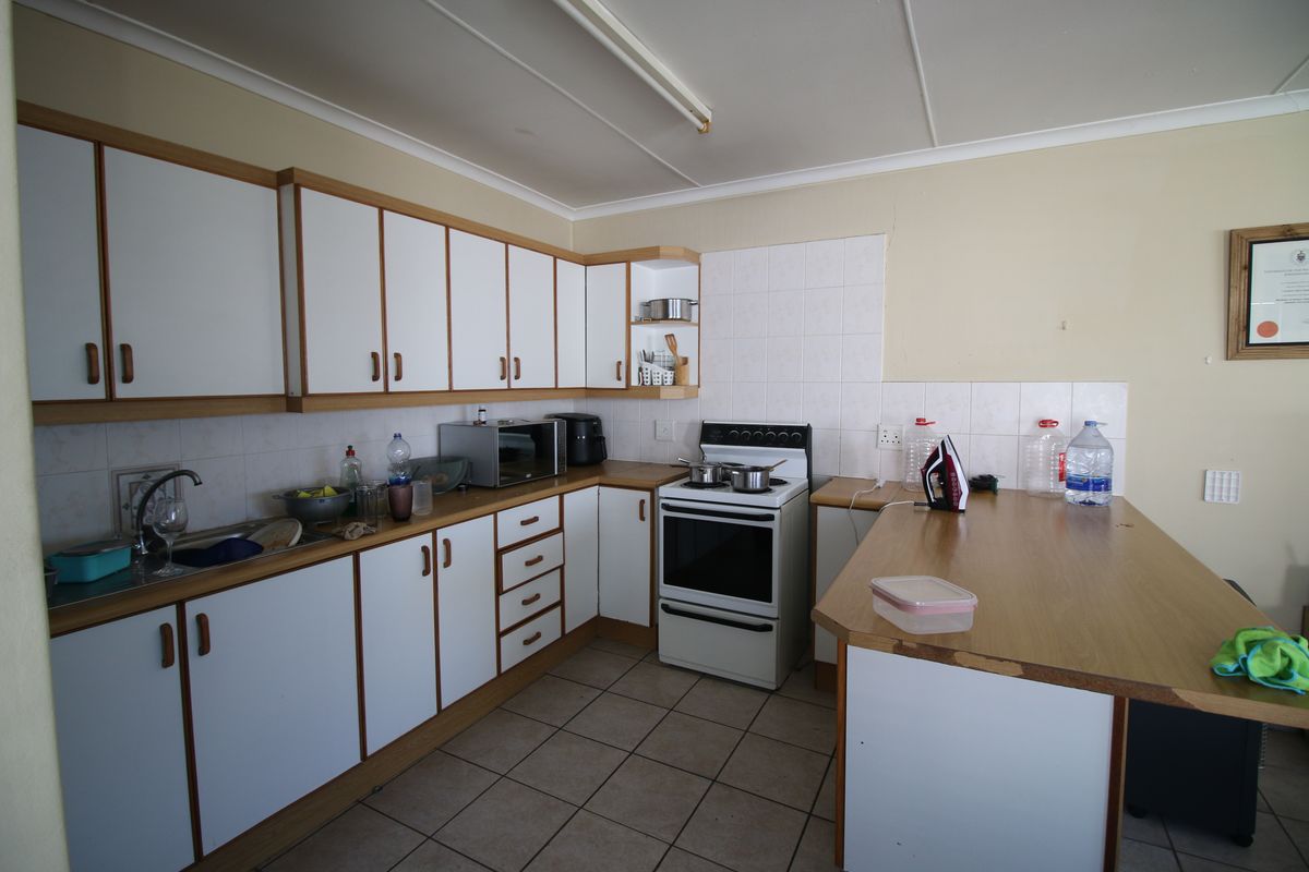 A functional kitchen featuring white laminate cabinetry, tiled backsplash, and a freestanding stove, offering a practical layout with potential for cosmetic updates.