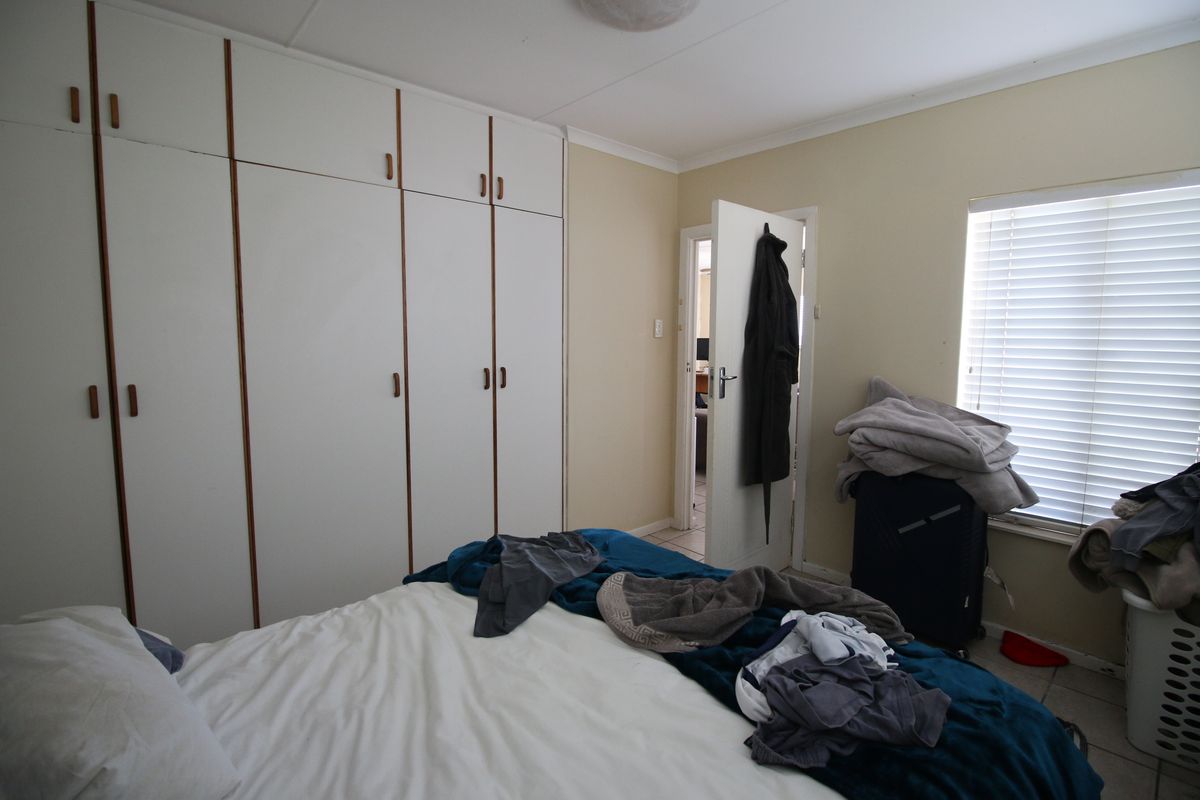 A functional bedroom featuring built-in cupboards, tiled flooring, and venetian blinds, offering a practical layout with neutral wall finishes.