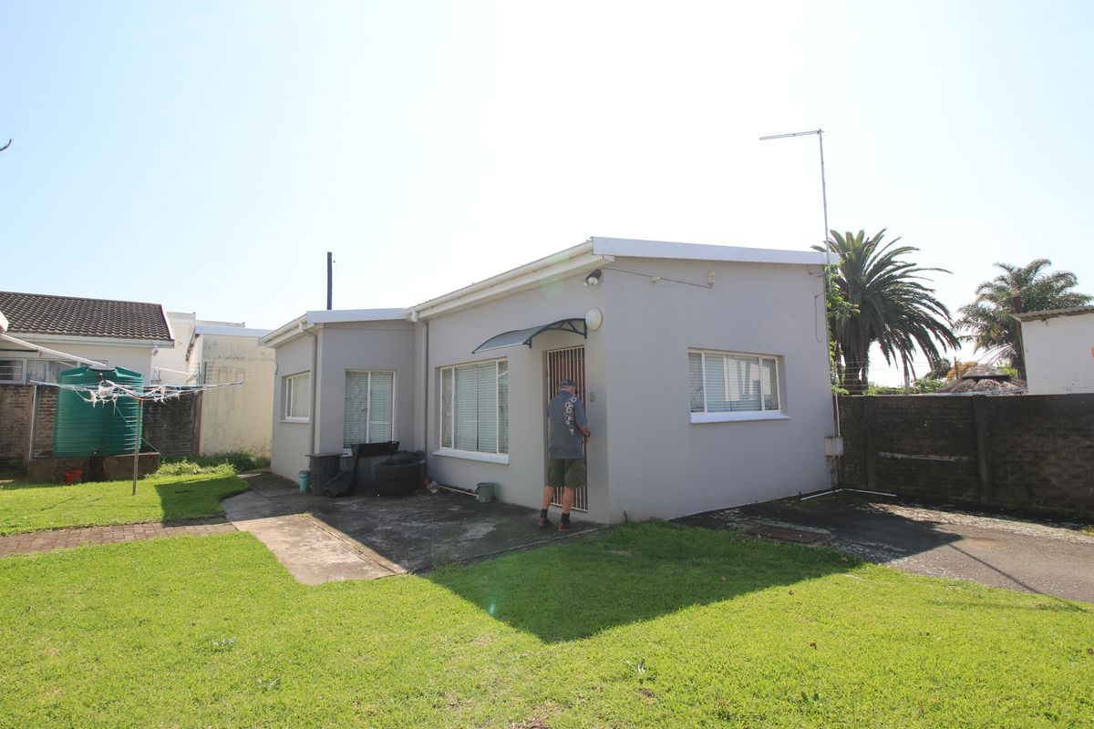 Rear view of the property featuring a concrete patio area, lawn, and perimeter brick boundary wall.