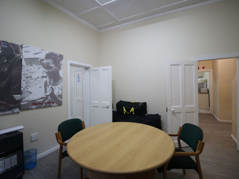 A functional room featuring a panelled ceiling, neutral walls, and multiple doorways leading to adjacent spaces, suitable for a home office or sitting area.