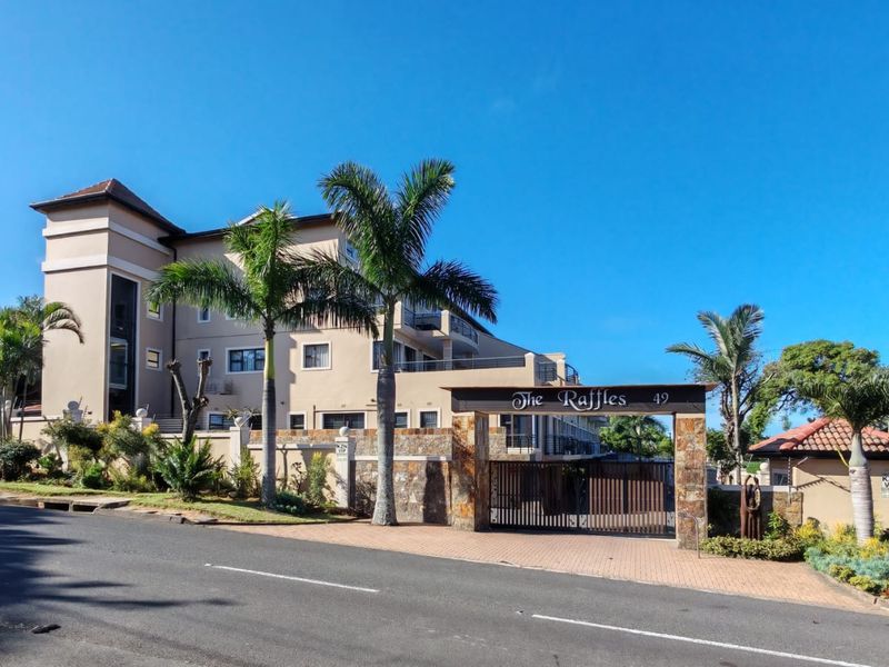 Street view of The Raffles apartment complex, featuring a secure gated entrance, stone-clad boundary walls, and well-maintained multi-story building architecture.