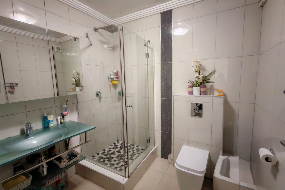 A modern bathroom featuring a glass shower enclosure, wall-mounted toilet with concealed cistern, and a contemporary glass vanity basin with tiled finishes.
