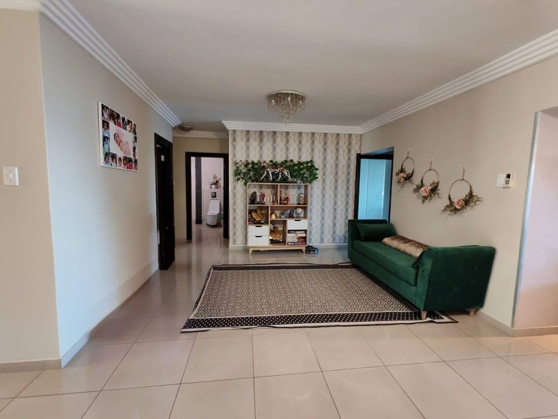 A spacious living room featuring neutral tiled flooring, decorative crown molding, and a stylish feature wallpaper wall with a central crystal chandelier.