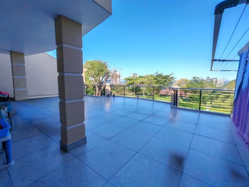 A spacious, covered balcony featuring tiled flooring and a metal balustrade, offering an open outdoor area with scenic views.