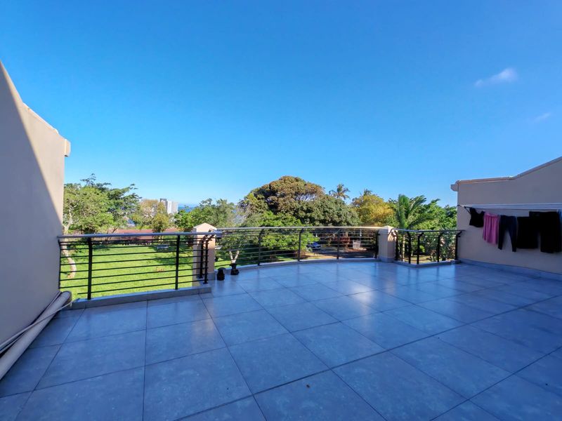 Spacious open-air balcony featuring tiled flooring and a metal balustrade, offering expansive views of the surrounding greenery and landscape.