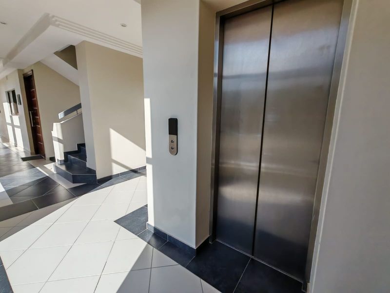 A clean and modern apartment building hallway featuring a stainless steel elevator, tiled flooring, and access to a staircase.