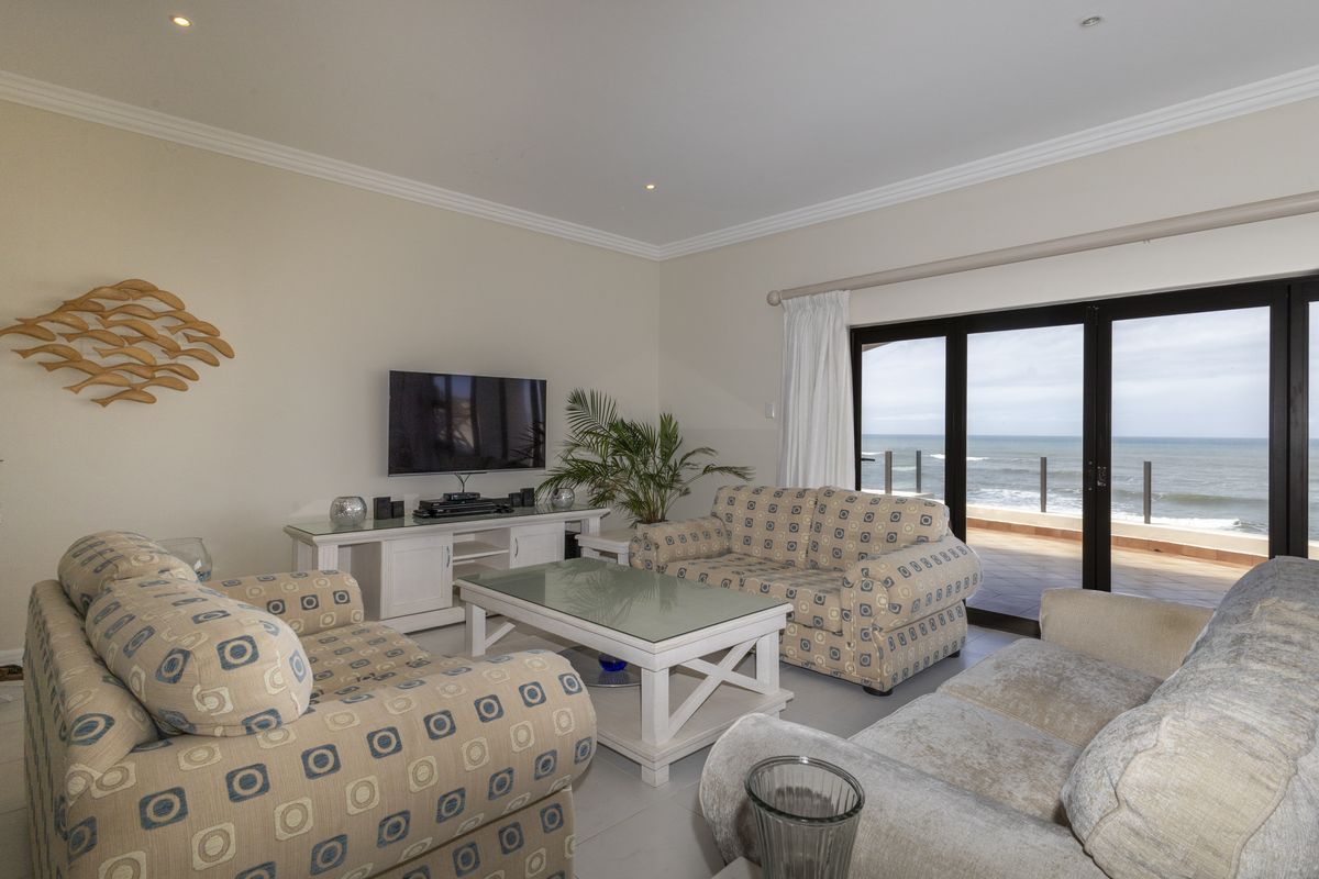 A bright living room featuring tiled floors, crown molding, and large sliding glass doors that open to a balcony with ocean views.