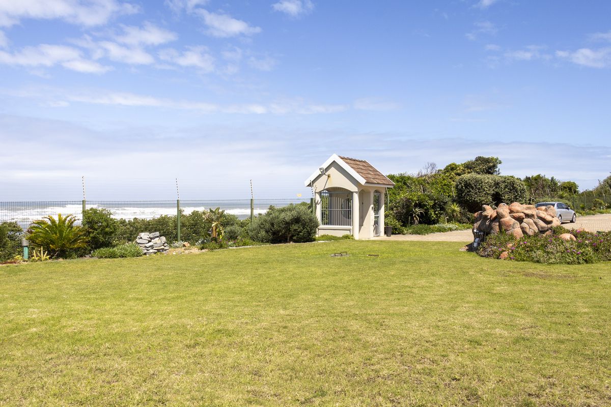 A well-maintained rear garden area featuring a security gatehouse, paved driveway, and electric fencing with a view towards the ocean.