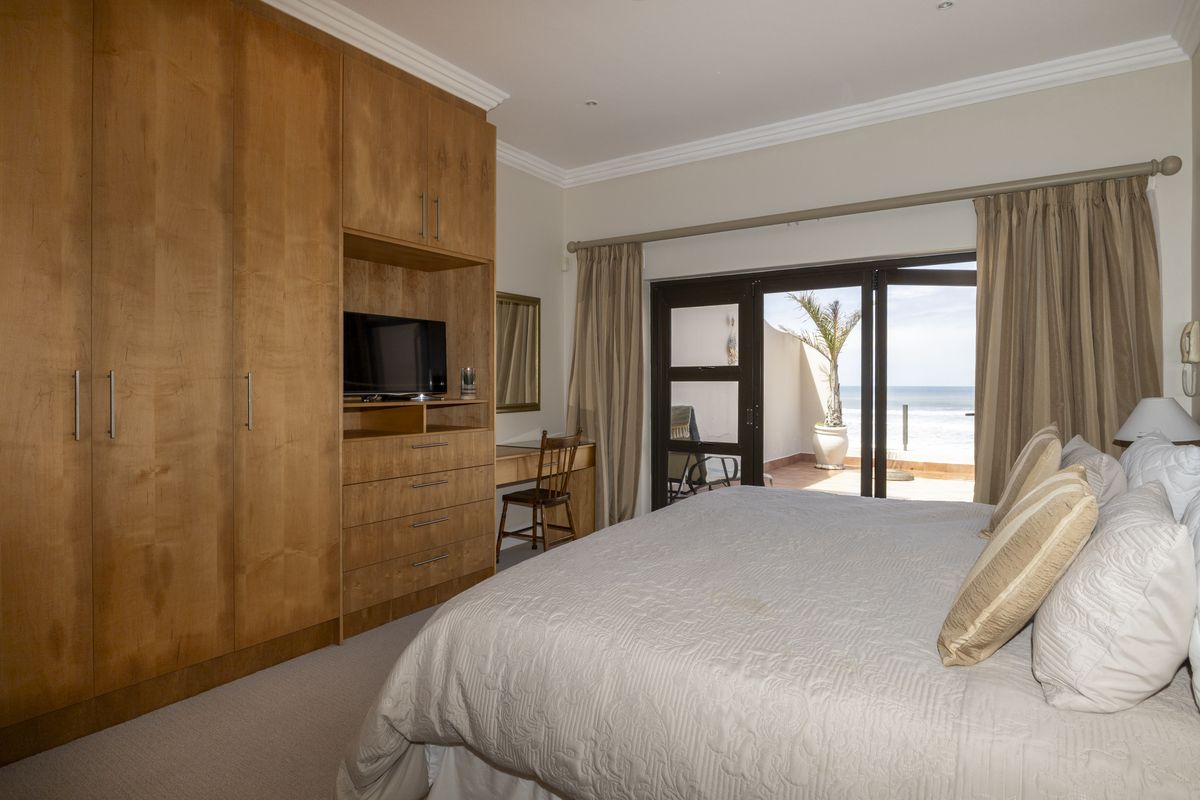 Spacious bedroom featuring extensive built-in wooden cabinetry, a vanity area, and sliding glass doors opening onto a private balcony with ocean views.