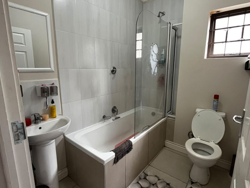 A functional bathroom featuring a pedestal basin, a bathtub with a glass shower screen, and a toilet, finished with neutral wall and floor tiles.