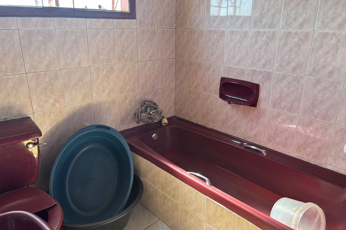 A dated bathroom featuring burgundy sanitaryware, tiled walls and floors, and a window with security bars. Ideal for a modern renovation.