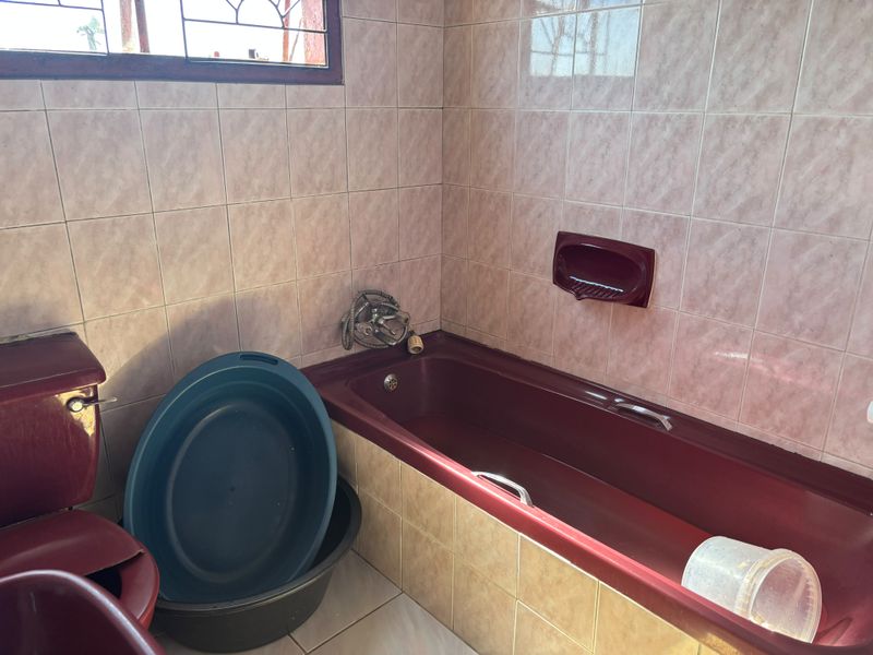 A dated bathroom featuring burgundy sanitaryware, tiled walls and floors, and a window with security bars. Ideal for a modern renovation.