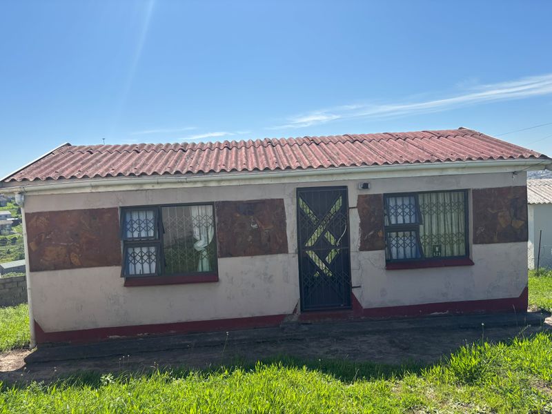 Front elevation of a single-story house featuring stone cladding accents, security gates, and burglar bars on windows with a corrugated roof.