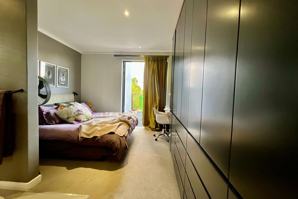 A well-lit bedroom featuring extensive floor-to-ceiling built-in cabinetry and direct access to a private balcony through a glass door.