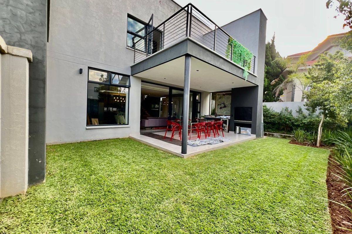Rear view of a modern two-story home featuring a covered patio, built-in outdoor braai area, and a balcony overlooking a landscaped garden.