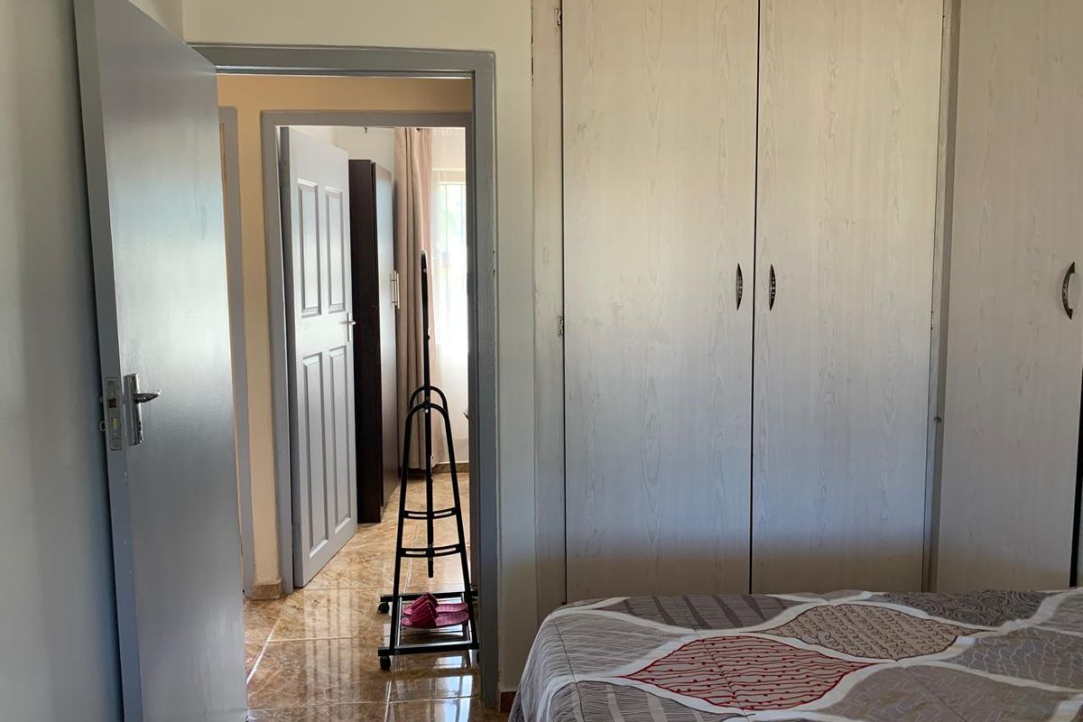 A bedroom featuring built-in cupboards and tiled flooring, with a view through the doorway into an adjacent room.