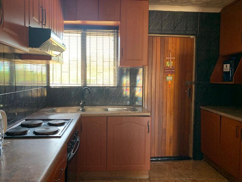 A functional kitchen featuring wooden cabinetry, laminate countertops, a built-in electric hob with extractor fan, and a tiled backsplash.
