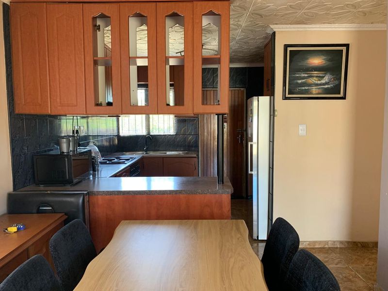 Open plan kitchen and dining area featuring wooden cabinetry, laminate countertops, and a tiled backsplash, offering a functional layout for daily living.