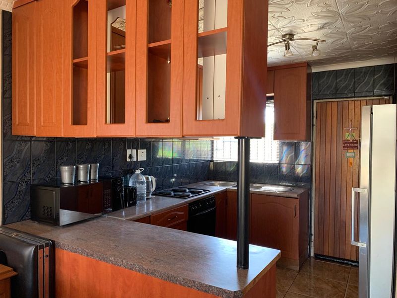A functional kitchen featuring wood-look laminate cabinetry, dark tiled backsplash, built-in cooking appliances, and a breakfast bar counter.