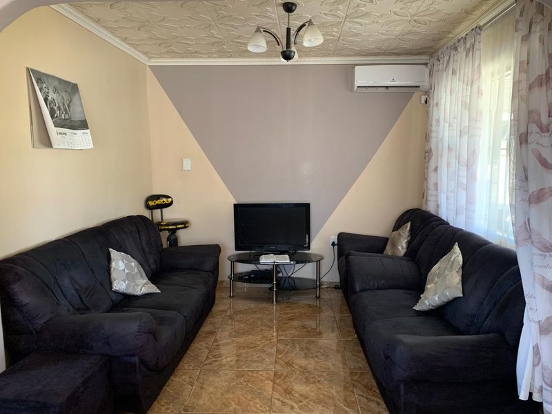 A living room featuring tiled flooring, decorative ceiling tiles, and a wall-mounted air conditioning unit.