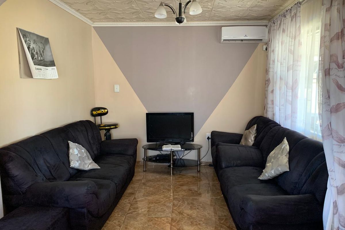 A living room featuring tiled flooring, decorative ceiling tiles, and a wall-mounted air conditioning unit.