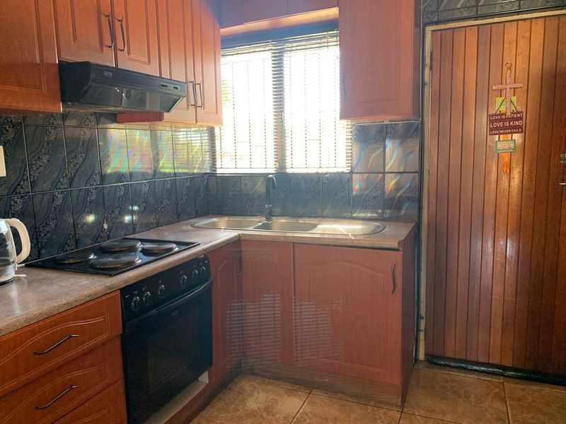 A functional kitchen featuring wooden cabinetry, laminate countertops, a built-in electric stove with extractor fan, and tiled finishes throughout.