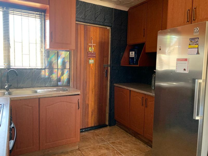 A functional kitchen featuring wood-look cabinetry, laminate countertops, a stainless steel sink, and tiled flooring with a side door access.