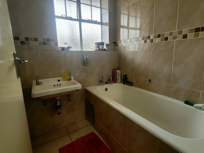 A functional bathroom featuring a built-in bathtub, wall-mounted basin, and neutral ceramic tiling throughout.