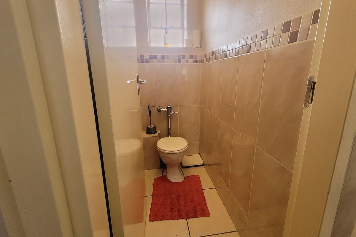 A compact guest bathroom featuring tiled walls with a decorative border, tiled flooring, and a window for natural light.
