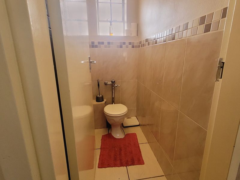 A compact guest bathroom featuring tiled walls with a decorative border, tiled flooring, and a window for natural light.