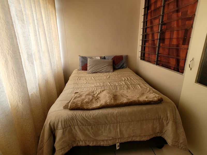 A compact bedroom featuring built-in cupboard storage and louvre windows, providing a functional and private sleeping space.