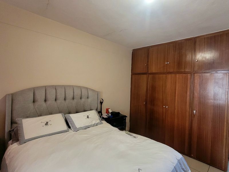 A bedroom featuring built-in wooden cupboards and tiled flooring, with an adjoining bathroom visible through the doorway.