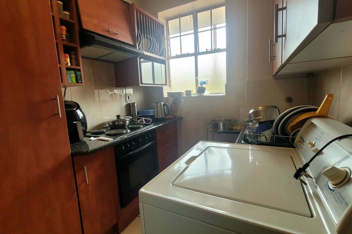 Compact kitchen featuring built-in wooden cabinetry, granite countertops, an electric hob, oven, and extractor fan, with a window providing natural light.