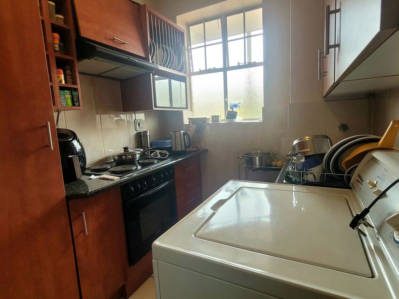 Compact kitchen featuring built-in wooden cabinetry, granite countertops, an electric hob, oven, and extractor fan, with a window providing natural light.
